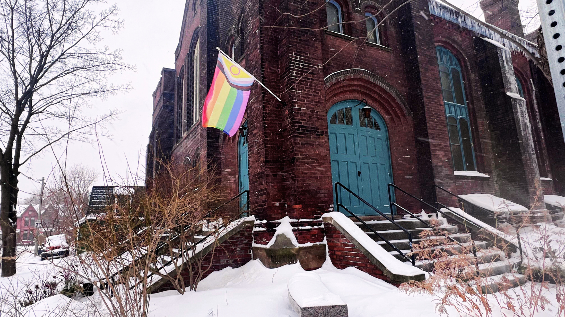 A snowy view of MCC Toronto, proudly displaying the Progressive Pride flag.